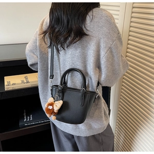 Side view of black pebble leather mini bucket bag with fuzzy brown butterfly charm