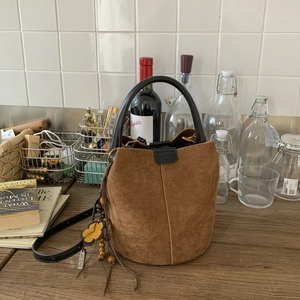 Close-up of brown suede bucket bag featuring contrast stitching and floral charm accessory