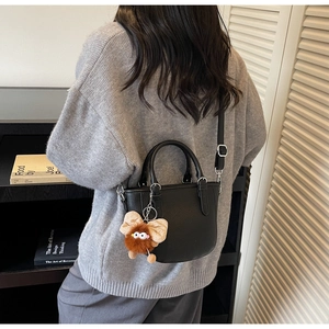 Close-up of black litchi grain leather bucket bag with a cute brown fuzzy monster charm