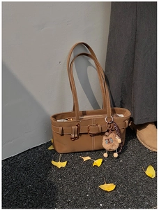 Brown vintage shoulder bag with buckle detail and plush charm on a street background
