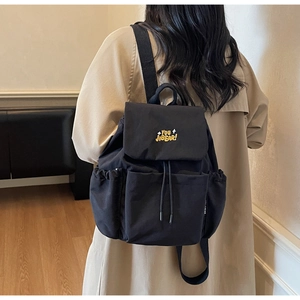 Detailed back view of a black canvas backpack with yellow embroidery and drawstring flap