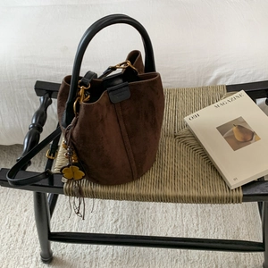 Detail of dark brown frosted bucket bag with leopard charm on a woven chair