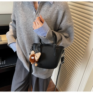Close-up of a black pebbled leather bucket bag with a brown plush bow charm on a model