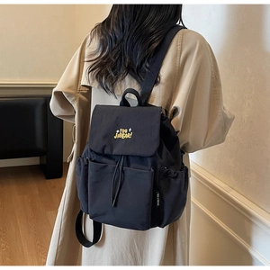 Detail of black canvas backpack showing yellow embroidery and drawstring flap closure