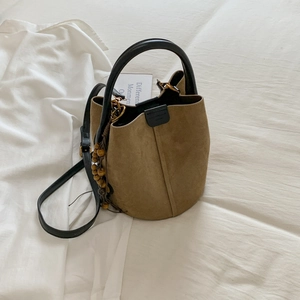Detail view of brown frosted suede bucket bag with black leather handles and wood bead charm