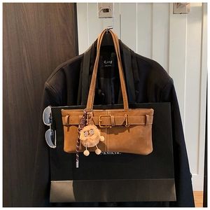 Detail view of brown suede underarm bag with belt buckle and cute plush lion charm