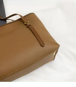 Macro shot of brown lychee-patterned leather tote with golden metal feet and fine stitching