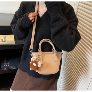 Detail of beige lychee pattern leather tote bag with a cute brown plush monster charm