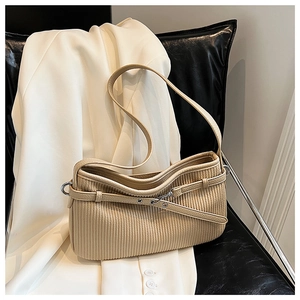 Detailed view of beige pleated shoulder bag with metallic buckle on a leather chair