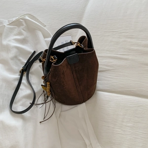 Close-up of brown suede bucket bag featuring drawstring and wood bead tassel detail