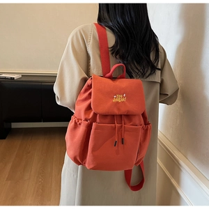 Rear view of a model wearing a large orange-red canvas backpack with embroidery detail