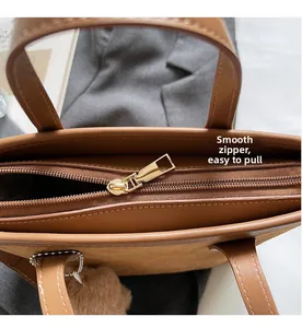 Close-up of smooth metal zipper closure on brown suede tote bag with plush ball charm