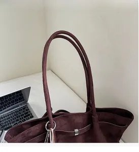 Gros plan sur la poignée robuste et la texture en daim bordeaux de ce sac à main chic