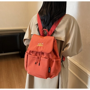 Detail of orange canvas backpack showing the embroidered flap and side pocket