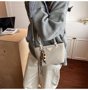 Close-up of cream quilted bucket bag with triangular plaque and beaded tassel detail