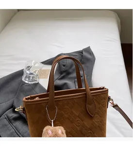 Close-up of brown suede tote bag with embossed circular patterns and plush cat ear charm