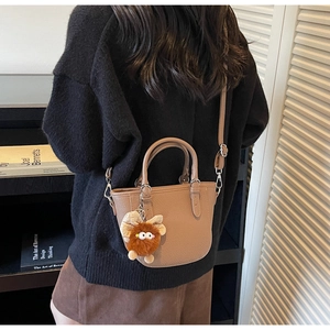 Close-up of a mini brown leather tote bag featuring a cute plush monster charm and fine texture