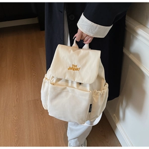 Detail of light beige canvas backpack featuring yellow embroidery and side pockets