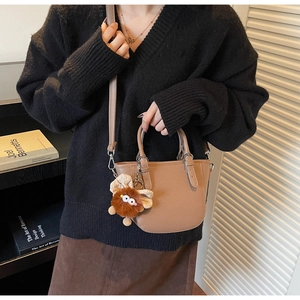 Close-up of brown pebbled leather mini handbag with long strap and cute plush monster charm