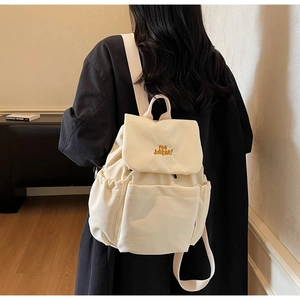 Minimalist canvas backpack shown in use with adjustable straps and yellow letter embroidery