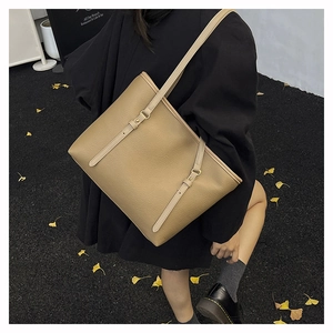 Close-up of khaki leather tote bag with gold buckles on an autumn street background