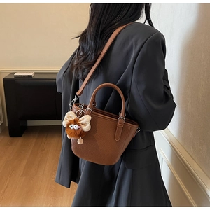 Detailed texture of brown lychee grain bucket bag with a cute plush monster charm