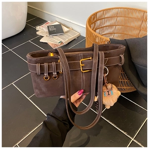 Detail of dark brown suede bucket bag with gold buckle and plush lion pendant charm