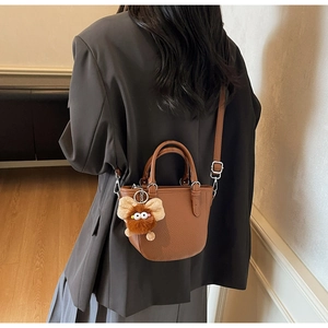 Brown litchi grain mini handbag styled with a plush doll charm on a grey suit outfit