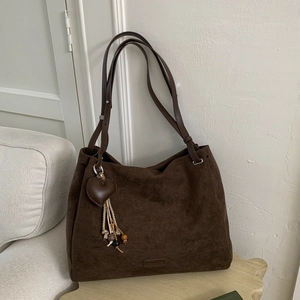 Detail of dark brown matte suede tote bag featuring heart charm and fringe tassel