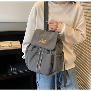 Detail of grey nylon backpack featuring drawstring closure and brand embroidery on the flap