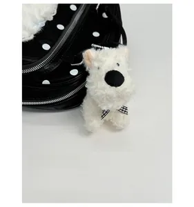 Close-up of fluffy white puppy plush keychain with a checkered bow on a polka dot bag