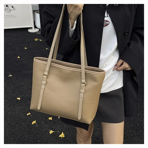 Close-up of khaki pebbled leather tote bag with gold buckles in outdoor autumn setting