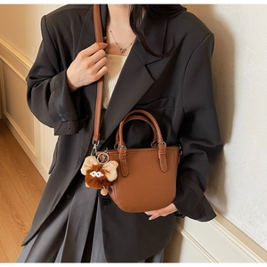 Close-up of brown pebbled leather tote bag with a cute monster plush charm and shoulder strap