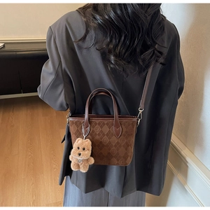 Close-up of brown quilted crossbody bag with plush bear charm and leather strap details