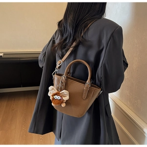 Brown lychee leather handbag with monster charm and adjustable strap shown on model