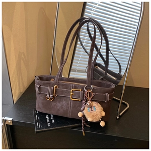 Detail of dark brown suede shoulder bag with contrast stitching and lion plush charm