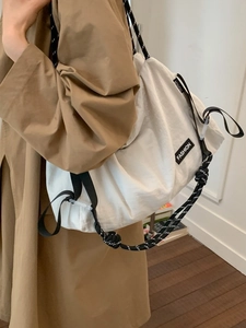 White minimalist canvas shoulder bag with woven strap shown on a model in a trench coat