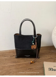 Detail of minimalist retro black suede bucket bag with leather flower charm on wooden table
