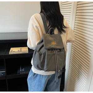 Detail of dark grey casual backpack featuring yellow letter embroidery and drawstring closure