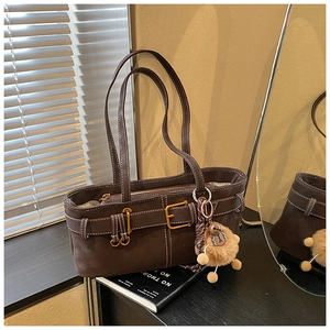 Close-up of brown suede bucket bag featuring leather buckle straps and cute plush bear charm