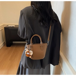 Detail of brown litchi leather bucket bag with cute plush pendant on grey blazer