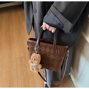 Detail view of brown faux suede bucket bag with checkerboard pattern and bear charm