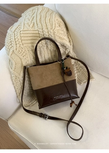 Retro two-tone leather handbag with adjustable strap and acorn charm on a soft sofa