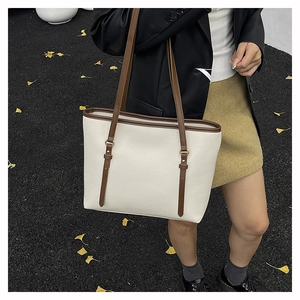 Detail of cream tote bag with brown straps and pebble leather texture on a shoulder