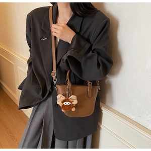 Detail of brown leather bucket bag with plush monster charm and silver metal hooks