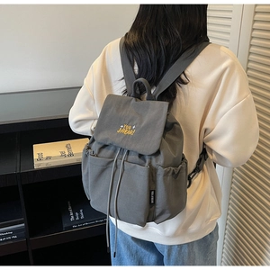Detail of grey drawstring backpack showing the flap embroidery and side storage pocket