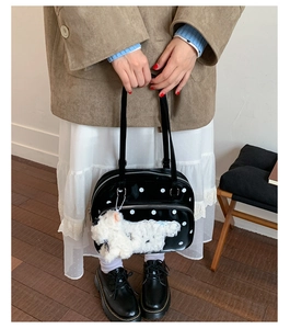 Detail of black polka dot patent leather handbag with a cute white plush puppy charm