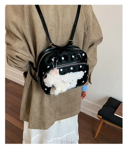 Detail of black polka dot backpack with plush puppy charm shown on model's shoulder