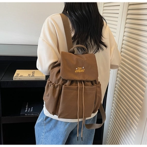 Detail of the brown canvas backpack showing the side drawstring pocket and embroidered logo