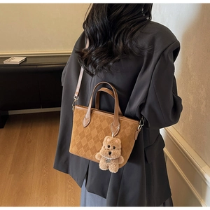 Detail of brown quilted tote bag featuring a plush bear charm and elegant shoulder strap